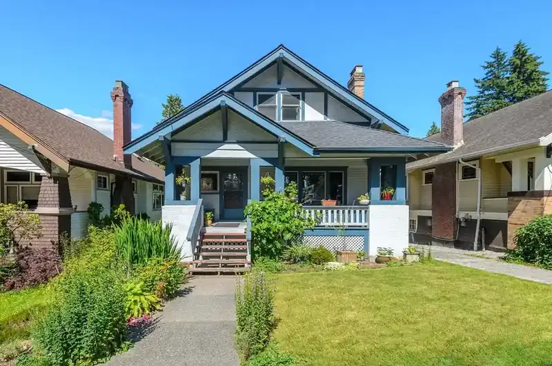 Blue Craftsman home photographed beneath a clear summer sky